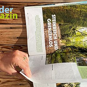 Sportpark Rabenberg EURORANDO 2026 Aussteller: OutdoorWelten GmbH Person mit Sportuhr liest Wander Magazin mit Artikel "Steinreich und grenzenlos"