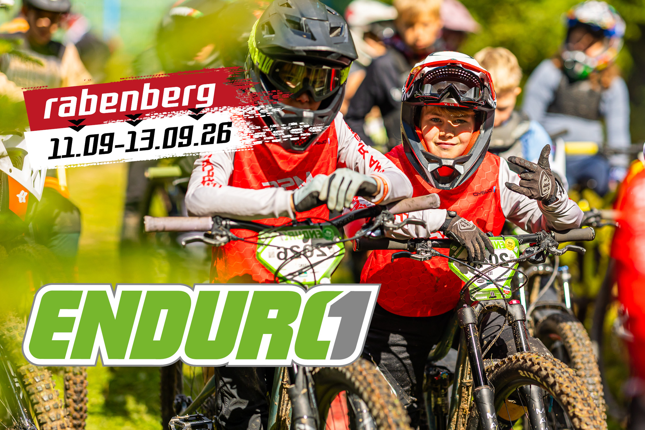 Sportpark Rabenberg Veranstaltungen: ENDURO1; © OCR BILDER Zwei junge Mountainbiker in voller Schutzausrüstung und roten Trikots vor dem Start, Logo "Rabenberg 11.09.-13.09.26" und "ENDURO1"