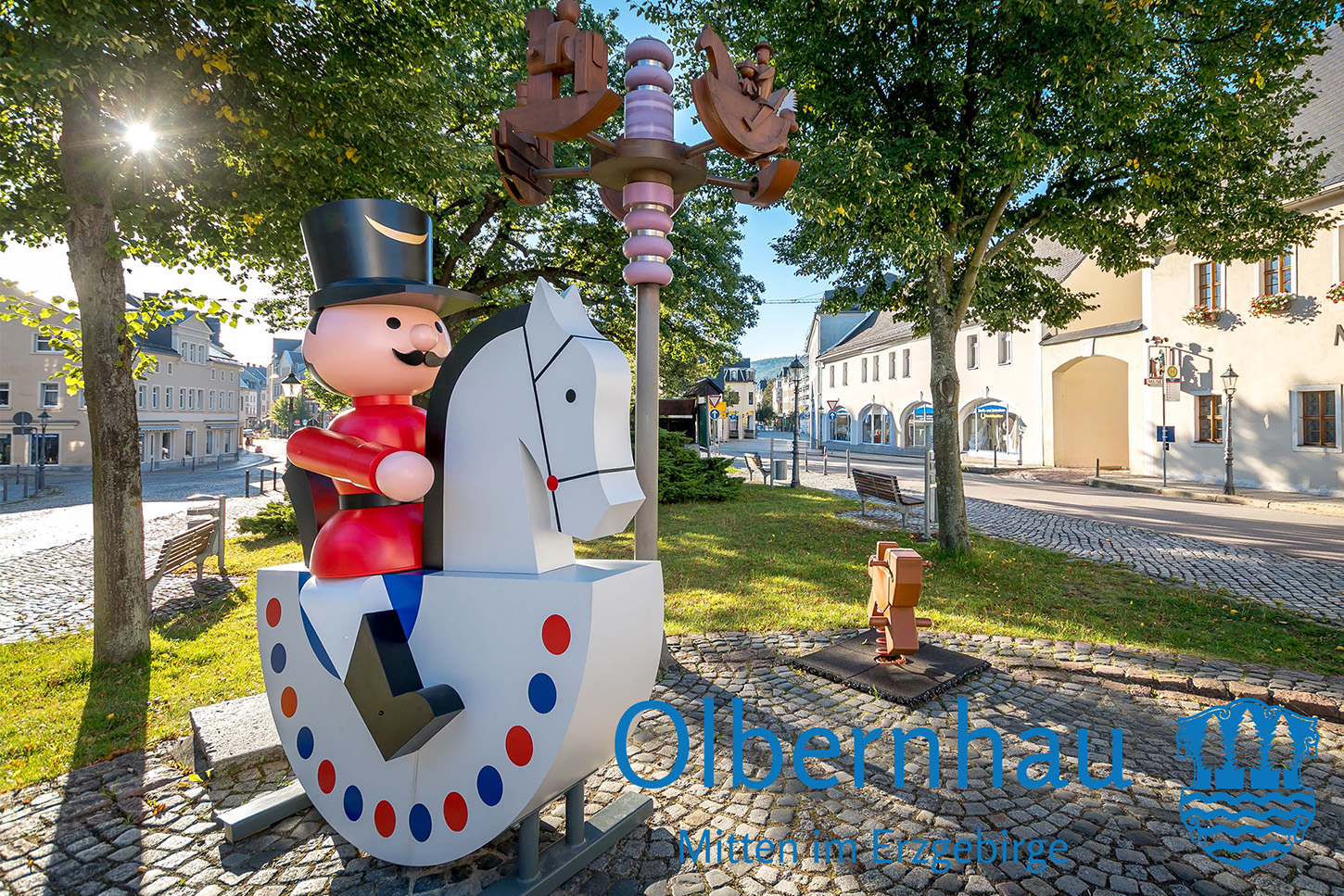 Sportpark Rabenberg EURORANDO 2026 Aussteller: Stadt Olbernhau; © KRISTIAN HAHN Dekorative Holzfigur eines Nussknackers auf einem Schaukelpferd-Sockel, Blaues Logo: Obernhau Mitten im Erzgebirge.
