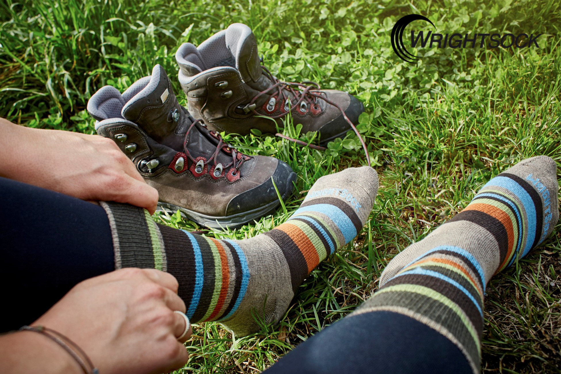 Sportpark Rabenberg EURORANDO 2026 Aussteller: WRIGHTSOCK Beine mit bunten Wandersocken und Wanderschuhe im Gras, eine Hand zieht eine Socke hoch.